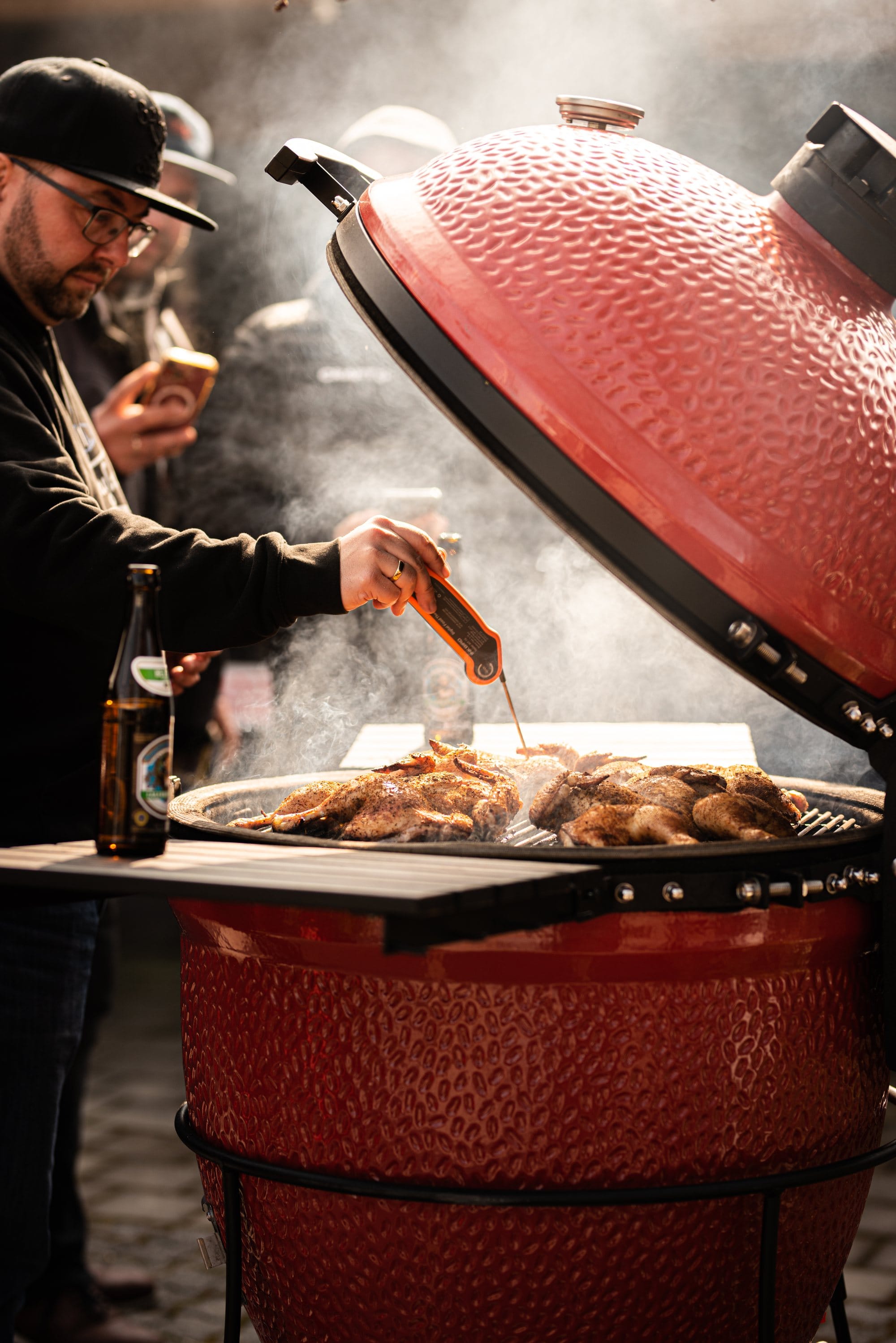 Sascha Lotzmann basting chicken over an open ceramic grill in heavy smoke